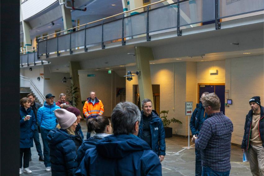Vinterkledde mennesker lytter til mann som viser dem rundt i et lyst lokale